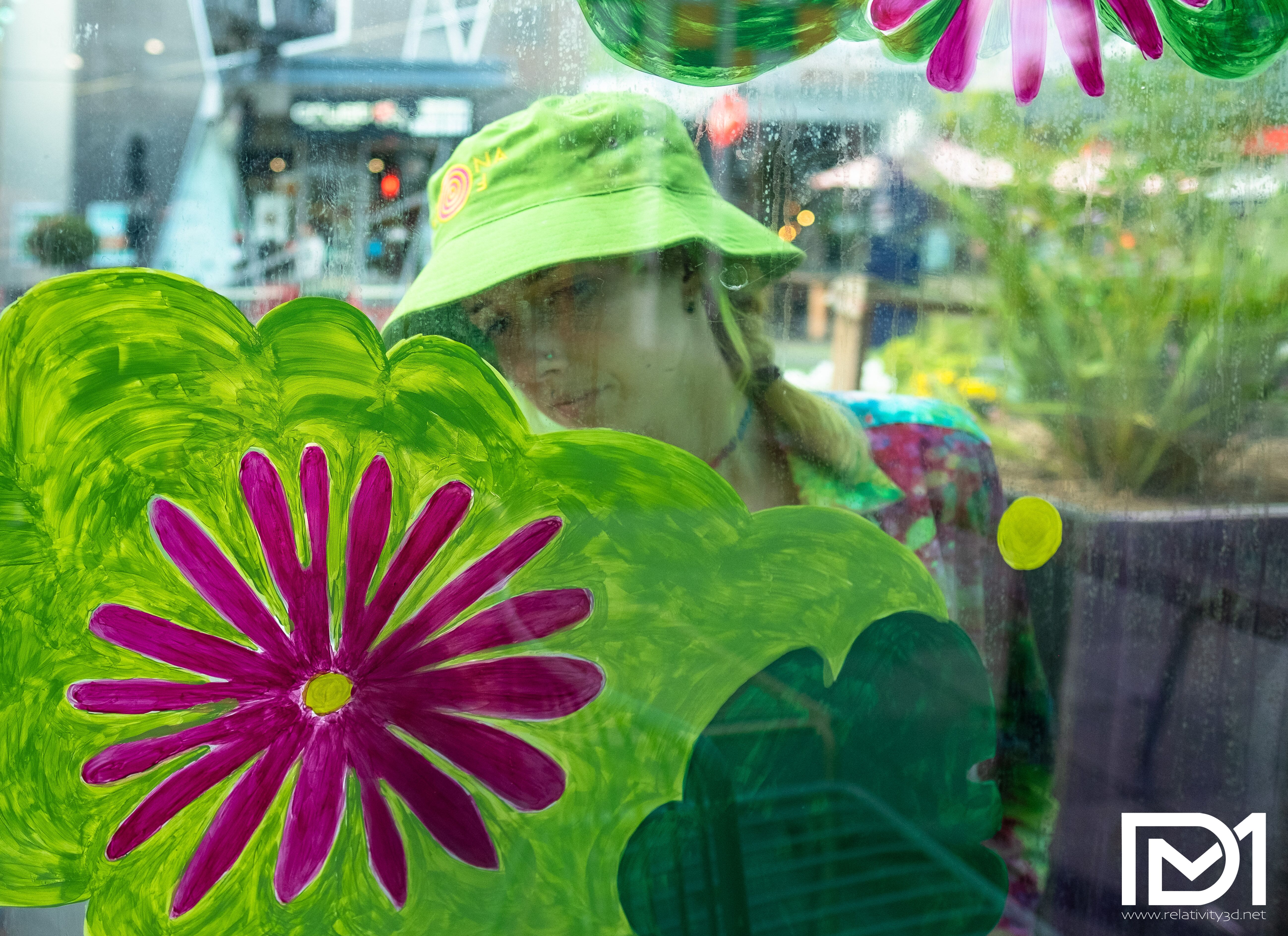Girl painting a flower on glass partition of outdoor seating along Murnong St.