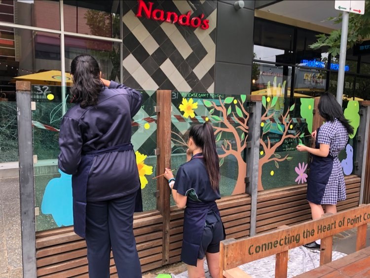 Primary school children painting on the glass partitions of restaurants and businesses on Murnong St.